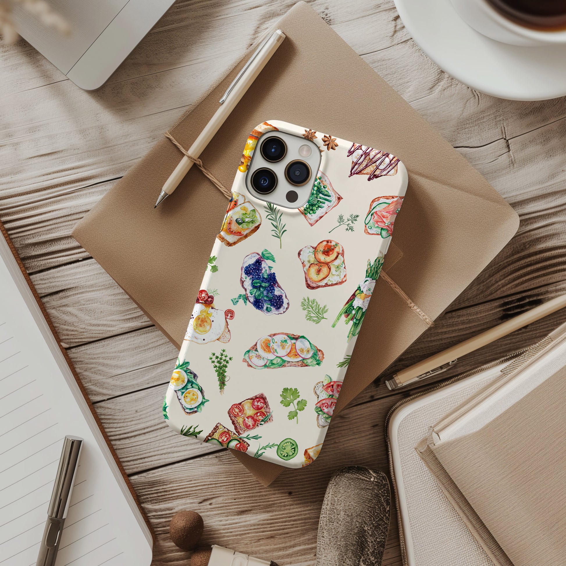 desk view of Sandwich Collage Phone Case is uniquely designed with delicate watercolor collage art. Available for both iPhone and Samsung Galaxy, this case artfully combines elements of open faced sandwiches with delicate herbs. Great foodie or chef gift by Artscape Market